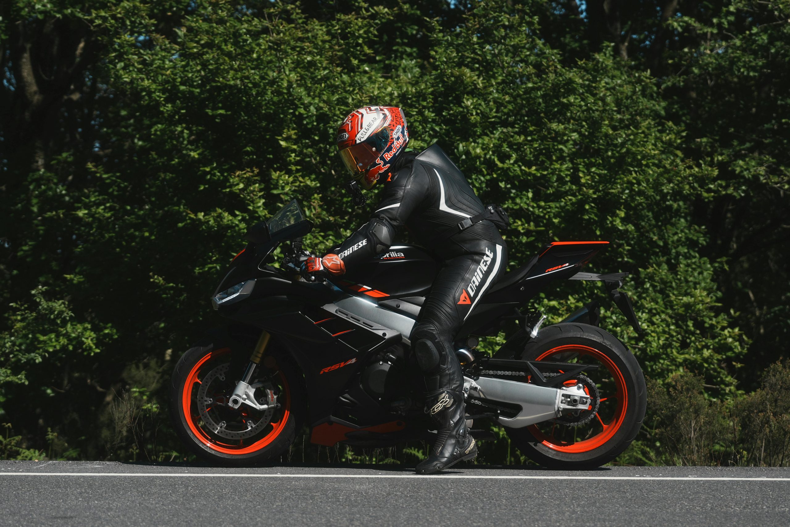 A motorcyclist on a sport bike rides through a scenic outdoor setting surrounded by lush greenery.